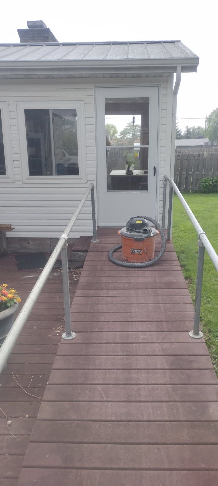 A wooden walkway leading to a white house with a vacuum cleaner in front of it.