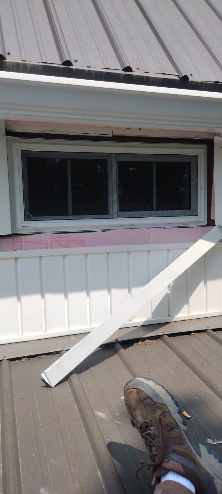 A person is standing on a roof next to a window.