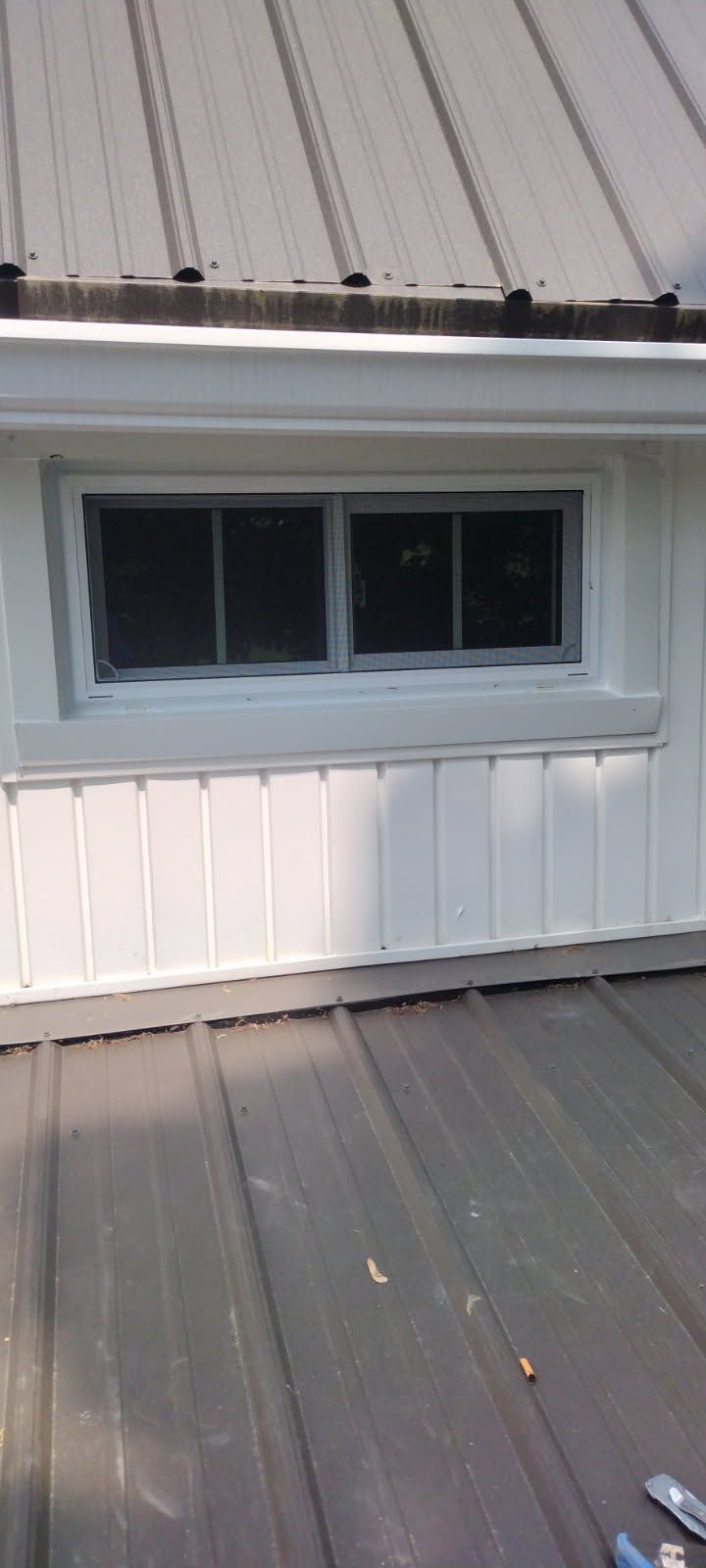 A window on the side of a building with a metal roof.