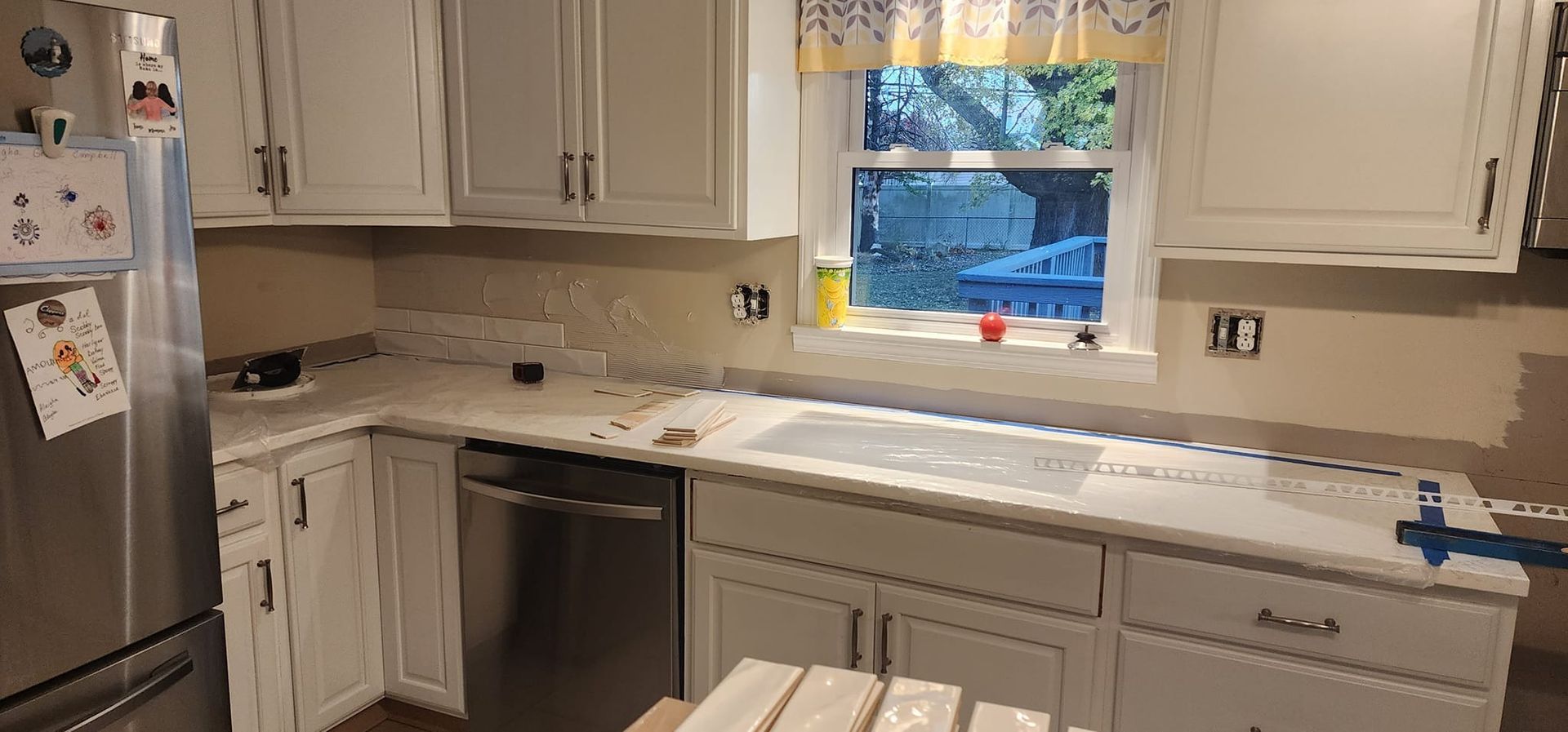 A kitchen with white cabinets , stainless steel appliances , and a window.