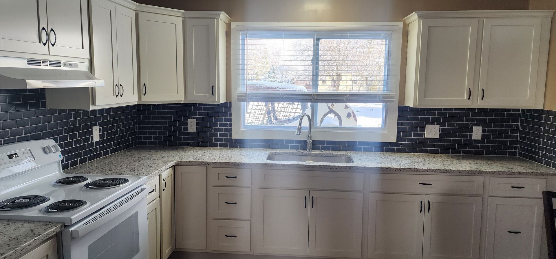A kitchen with white cabinets , granite counter tops , a stove and a sink.