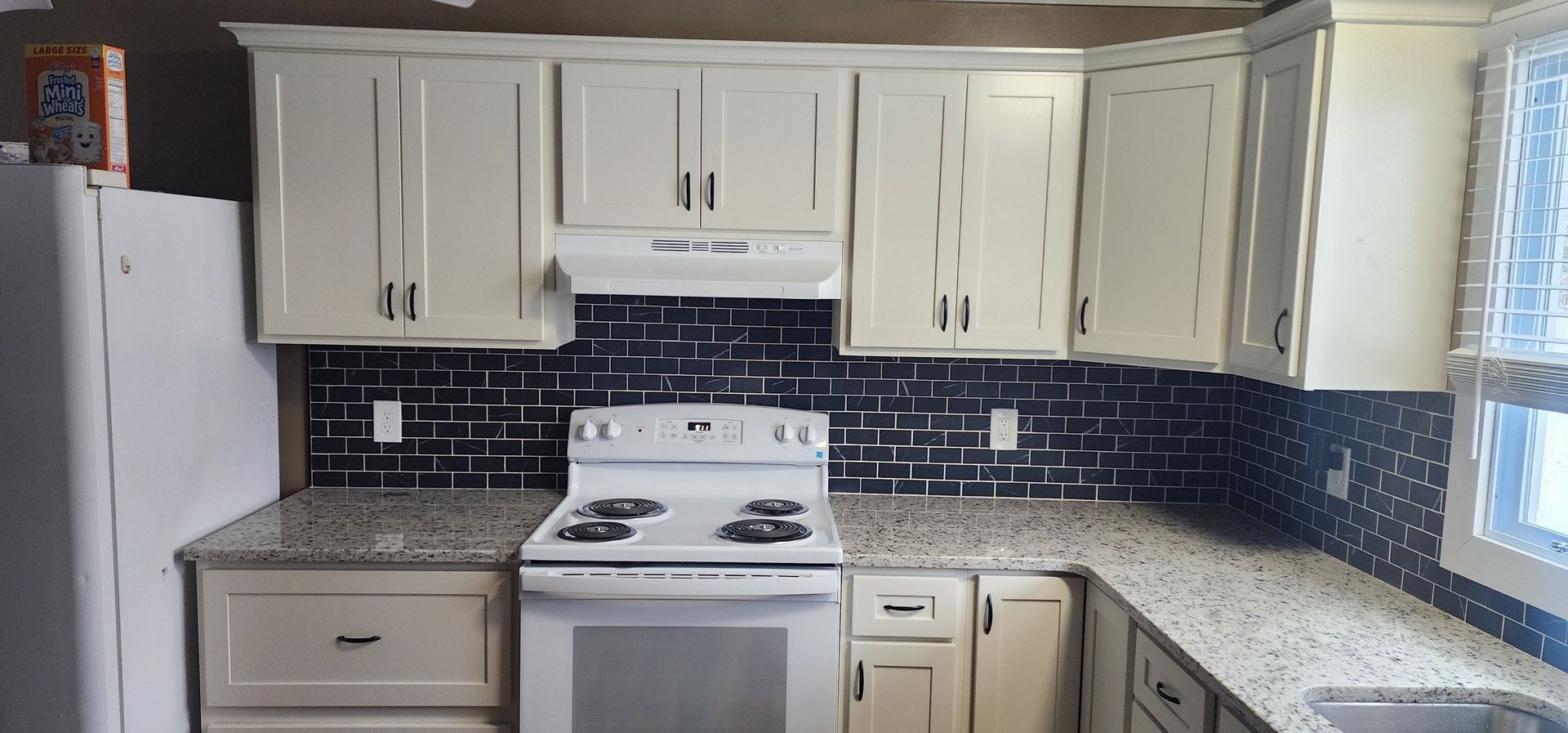 A kitchen with white cabinets , granite counter tops , a stove and a refrigerator.