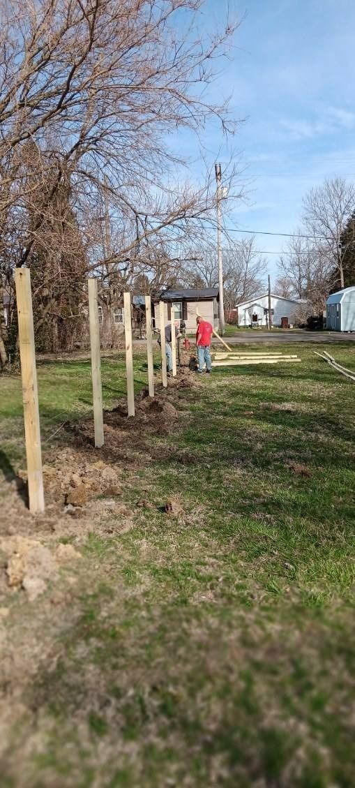 A man is standing in the middle of a grassy field next to a wooden fence.