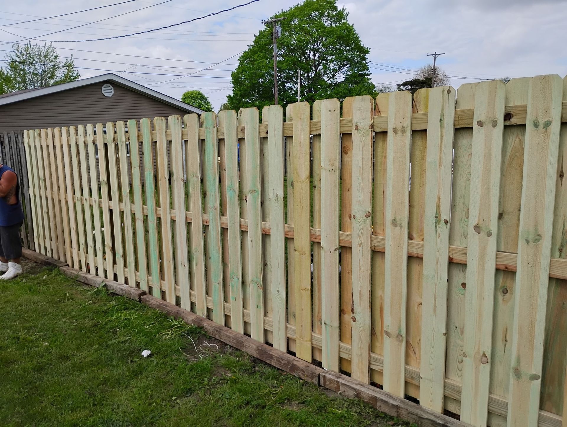 A man is standing next to a wooden fence in a yard.