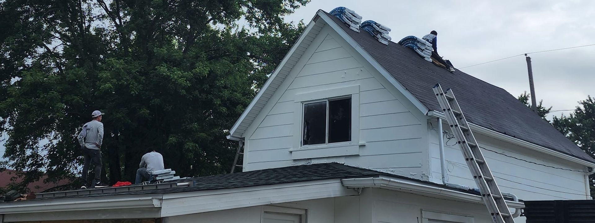 Two men are working on the roof of a white house.