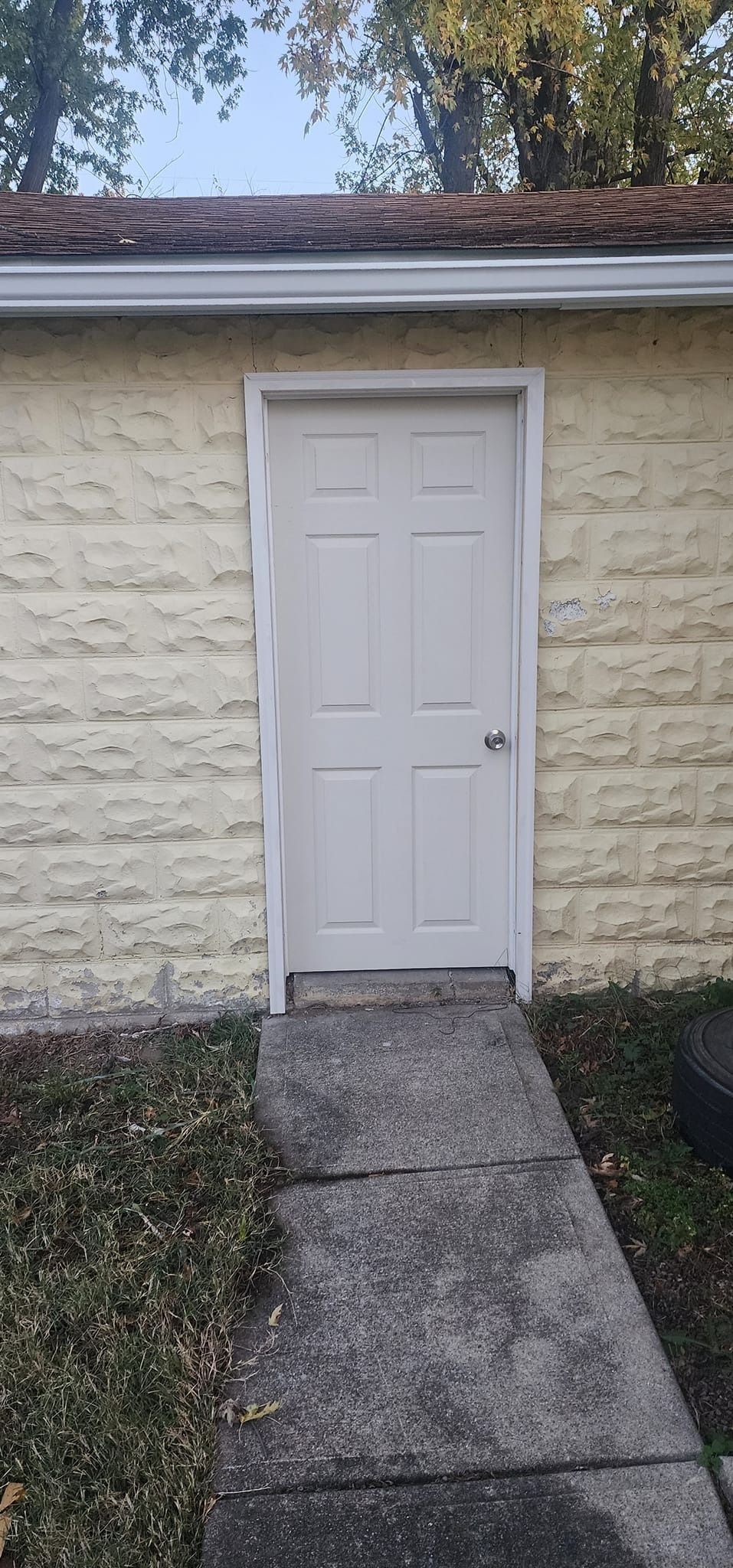 A white door is on the side of a brick building next to a sidewalk.