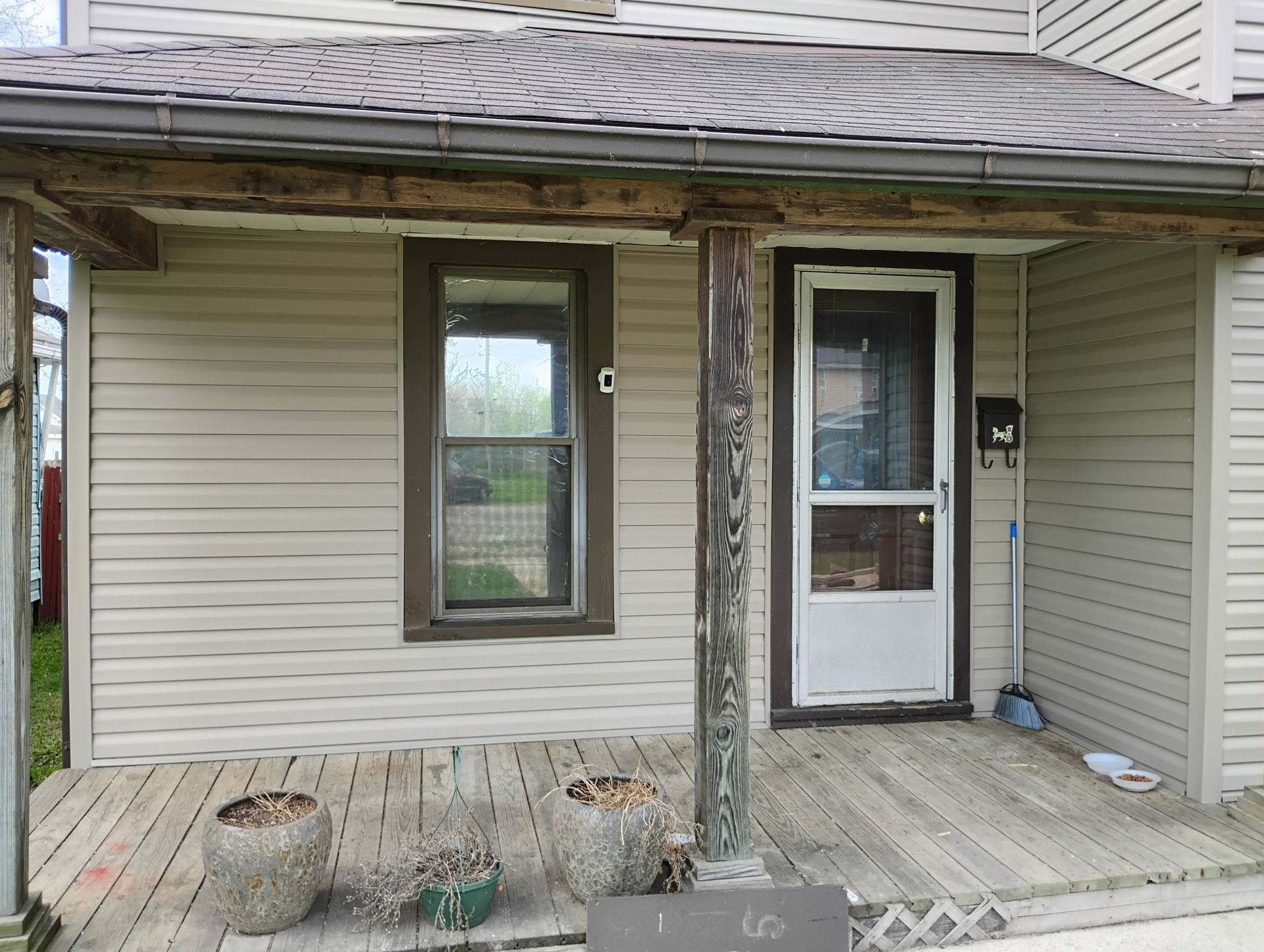 The front porch of a house with a screen door and a window.