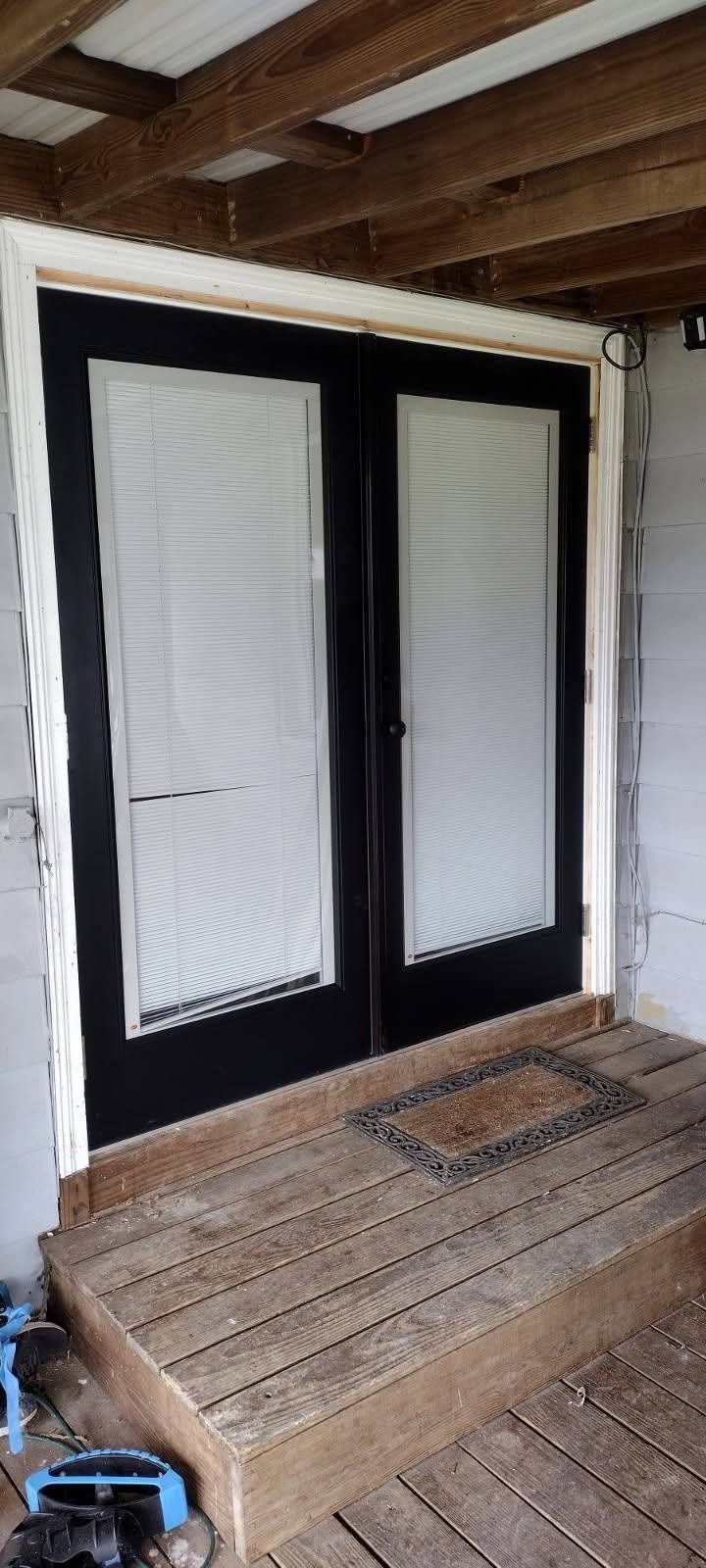A pair of black sliding glass doors are being installed on a wooden deck.