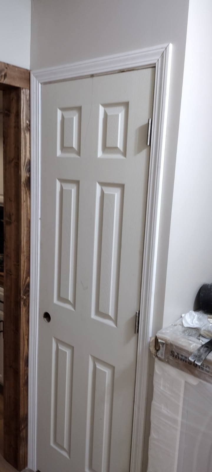 A white door is sitting next to a wooden door in a room.