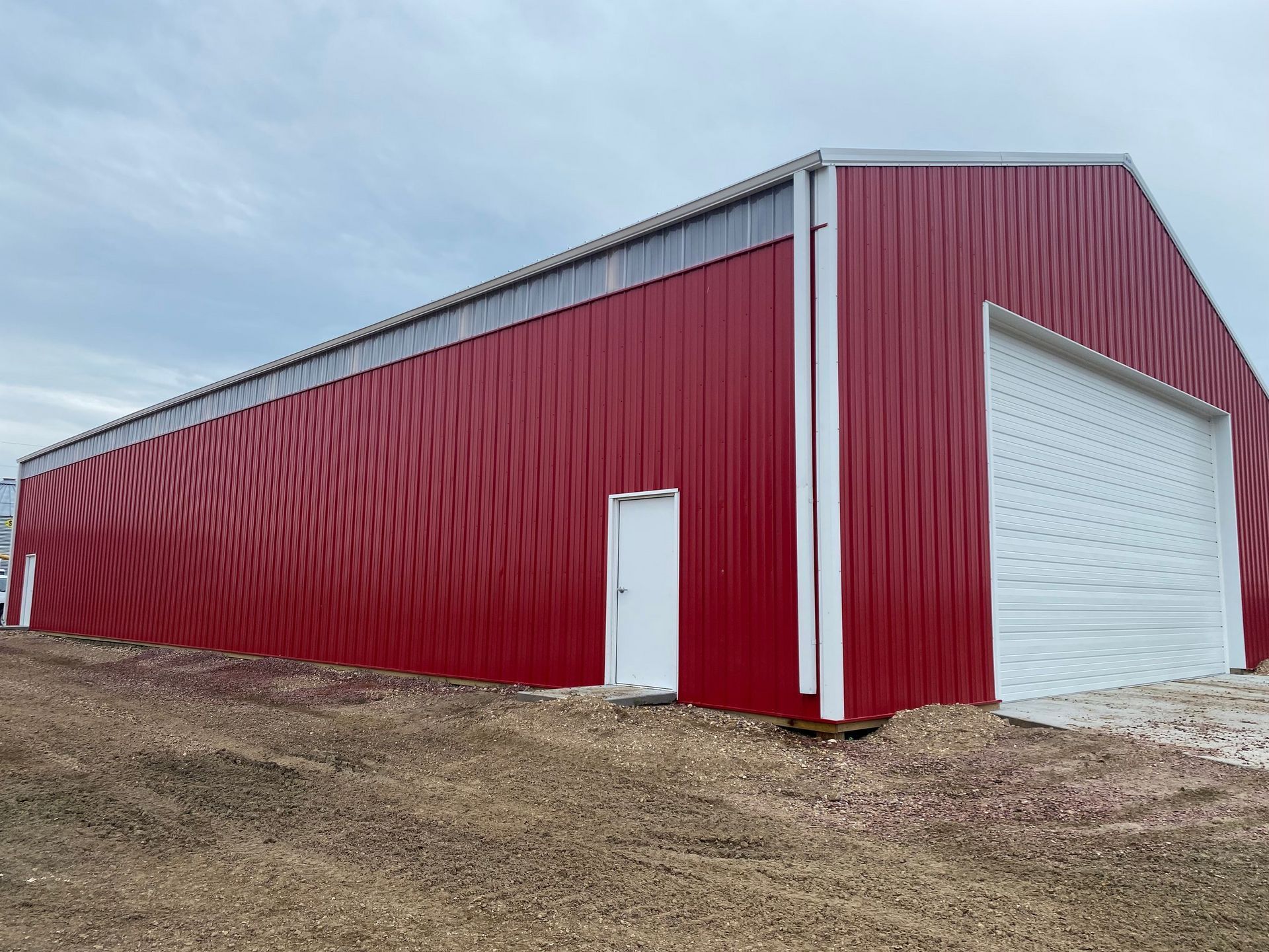 A large red building with a white garage door is sitting on top of a dirt field.