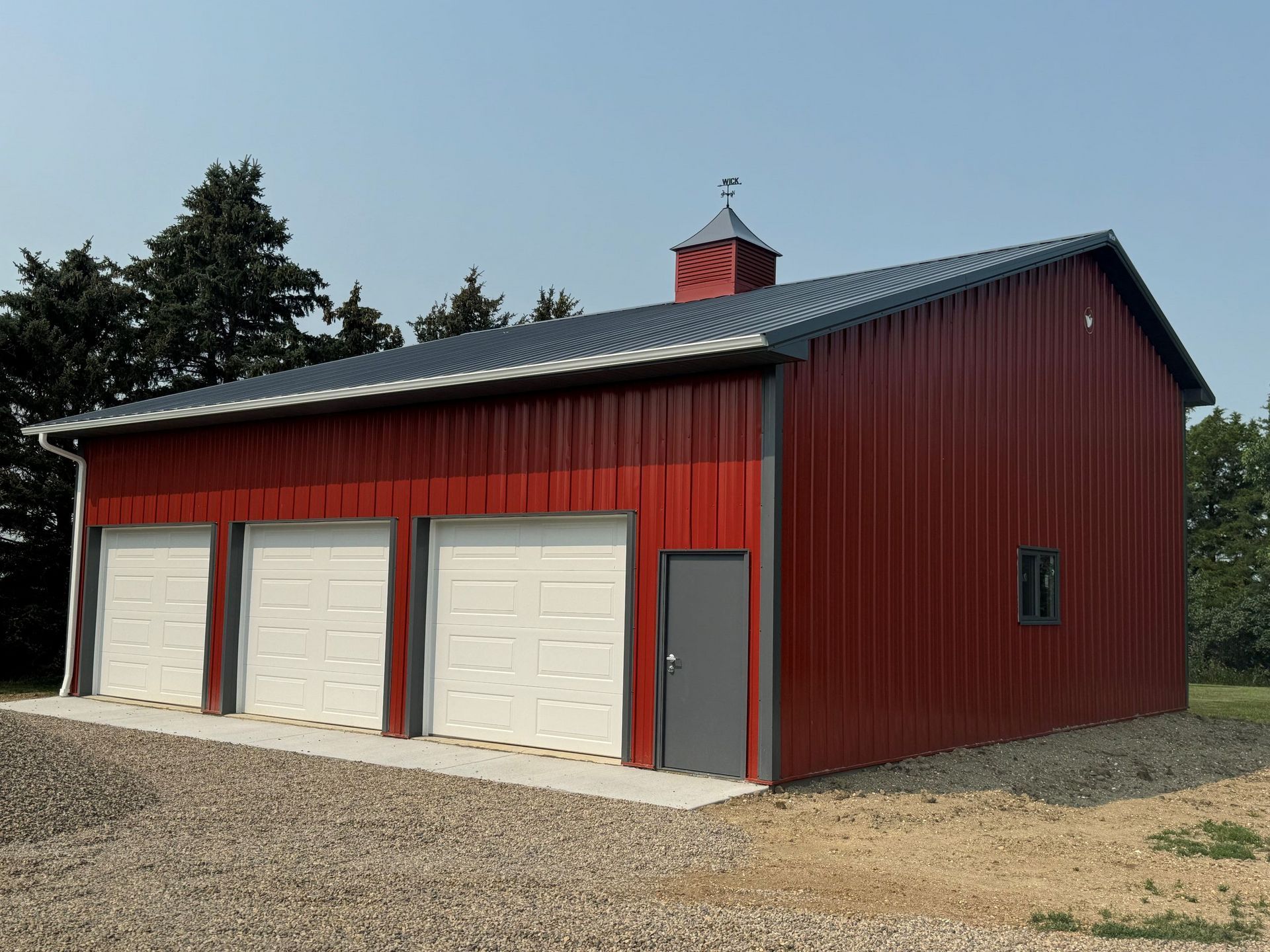 A red barn with three white garage doors and a black roof.