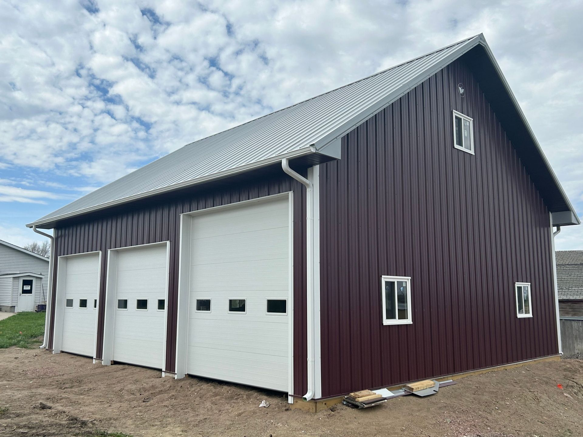 A red barn with white doors and windows is sitting on top of a dirt field.