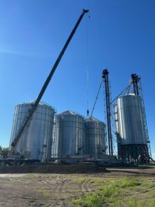 A large crane is standing in front of a row of silos.