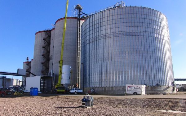 A large silo with a yellow crane in front of it