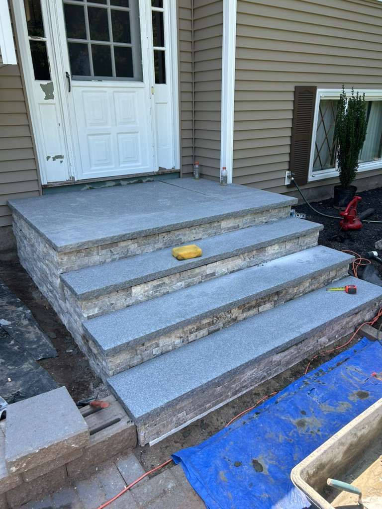 Front porch with newly built concrete steps, white door, and construction tools nearby
