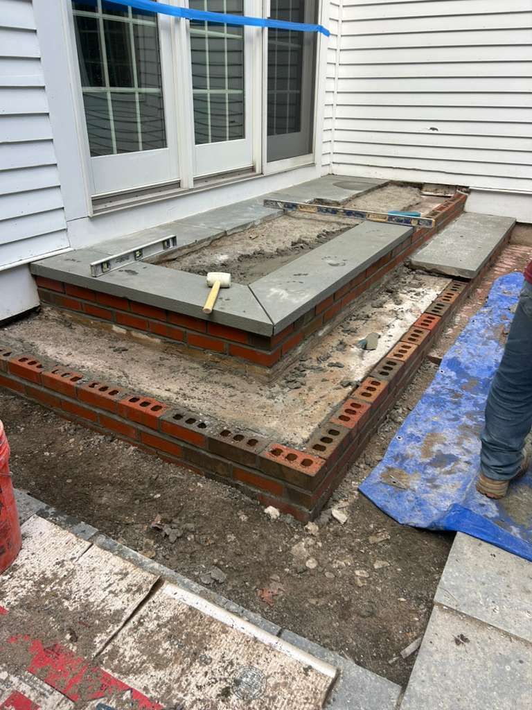 Concrete step under construction beside a house, with rebar, forms, and tools on the site.
