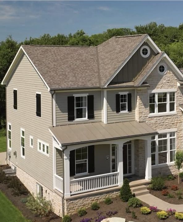 Two-story beige house with white trim, front porch, and landscaped yard under a blue sky