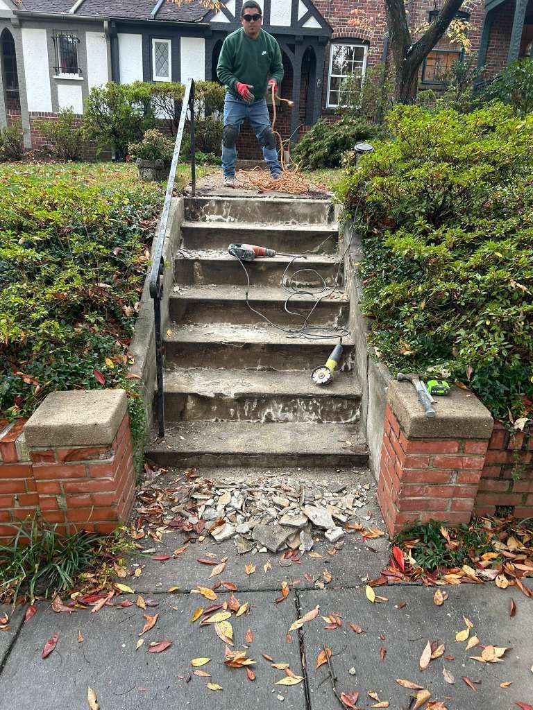 Damaged concrete steps between brick walls, with a person standing at the top and fallen leaves on the ground.