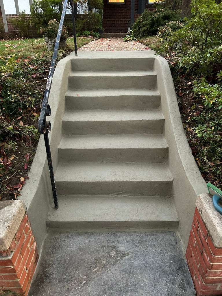Concrete outdoor staircase with five steps between brick side walls and black handrails.