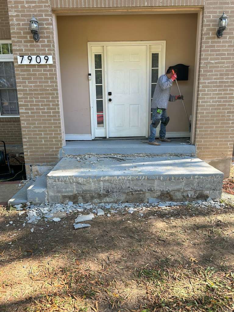 Person standing on cracked front steps beside a white door and brick house porch