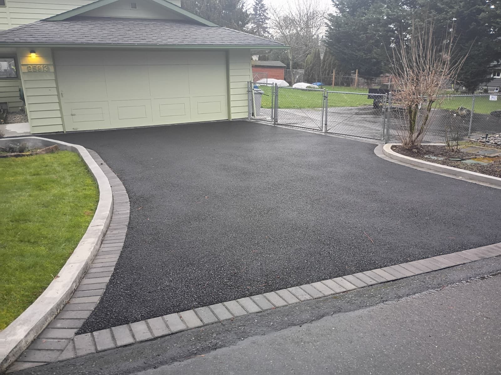 Freshly paved black driveway leading to a two-car garage with landscaped edging.
