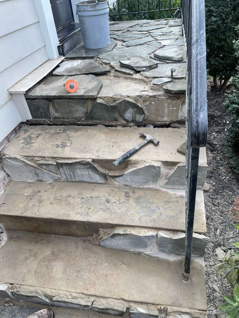 Stone front steps with a broken landing and loose handrail beside a house