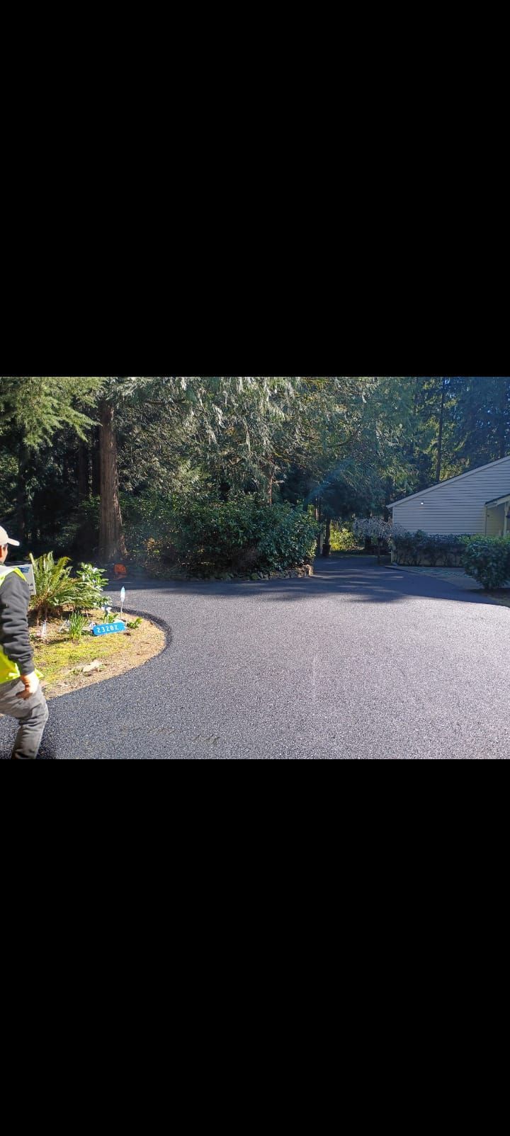 Sunlit gravel driveway curving past landscaped trees and a house with a garage