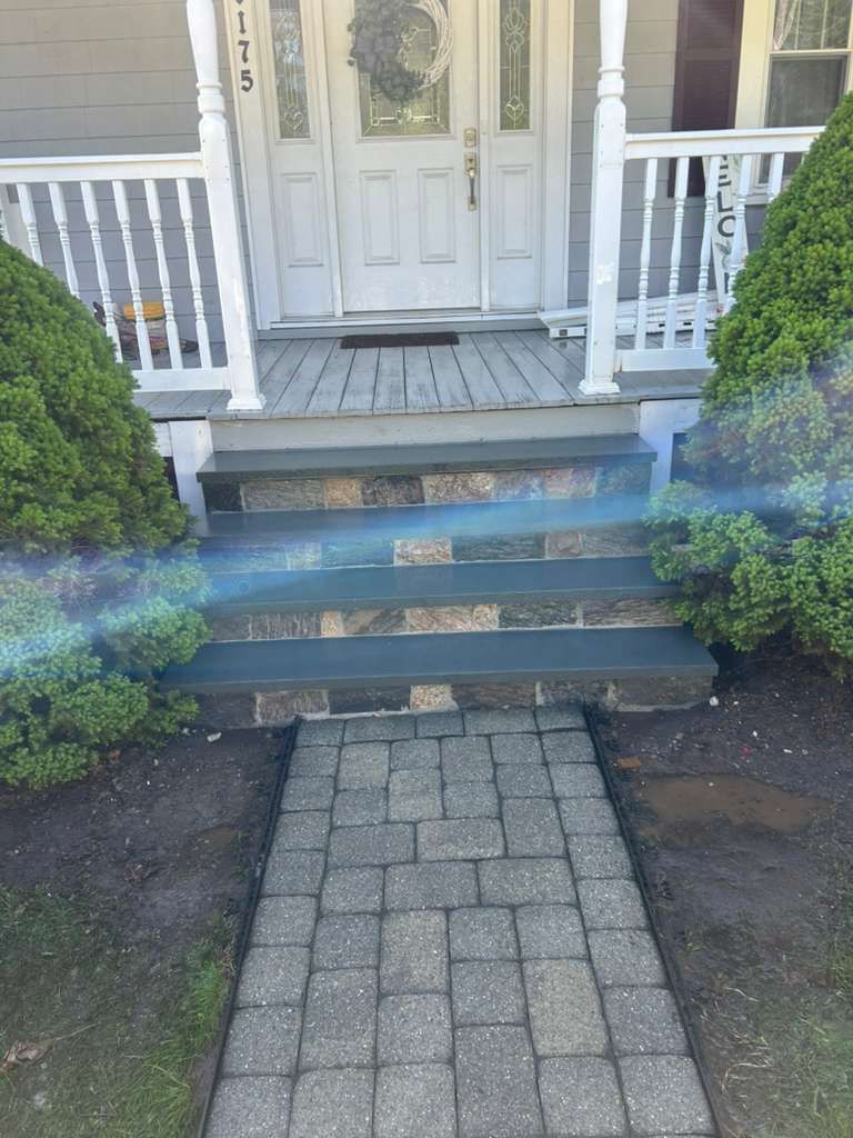 Front steps with blue-gray risers leading to a white front door and porch, bordered by shrubs.