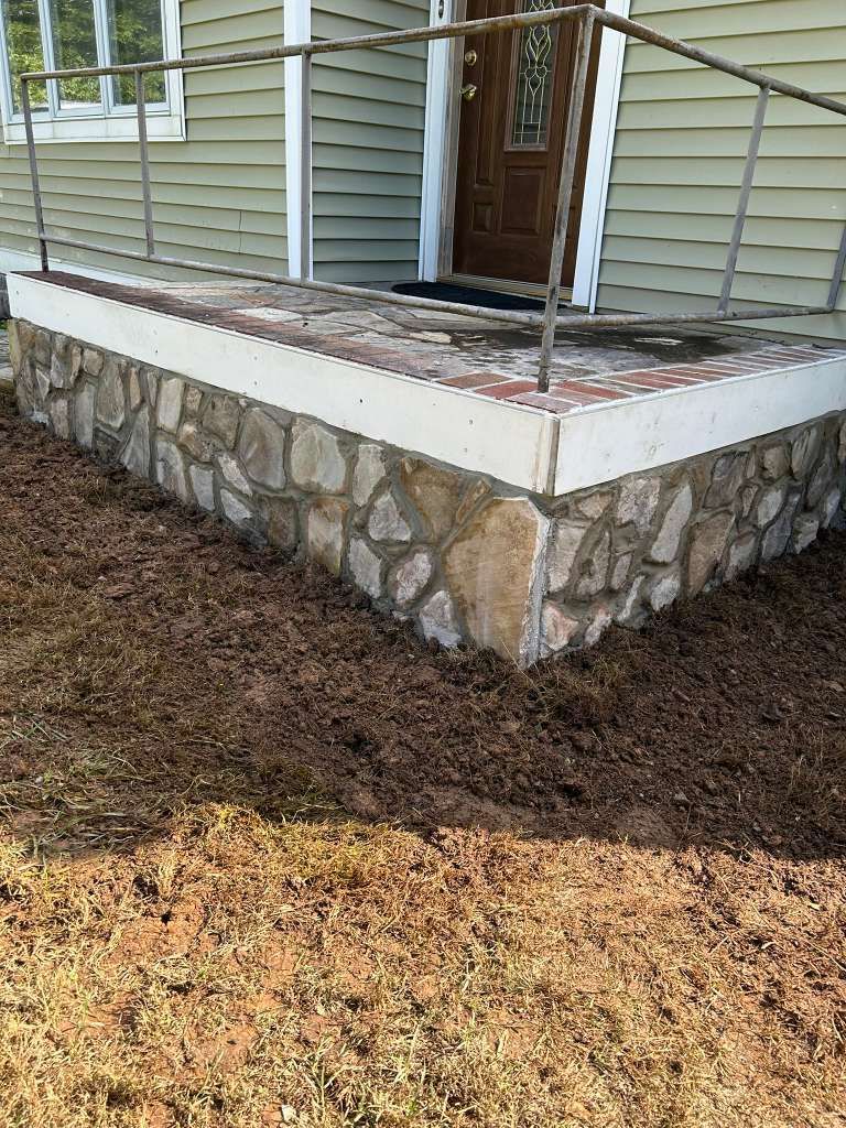 Stone porch with wooden railing and front door on a house exterior.