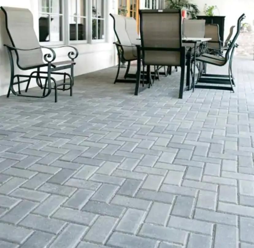 Patio with gray paver stones and outdoor chairs around a table beside a white house