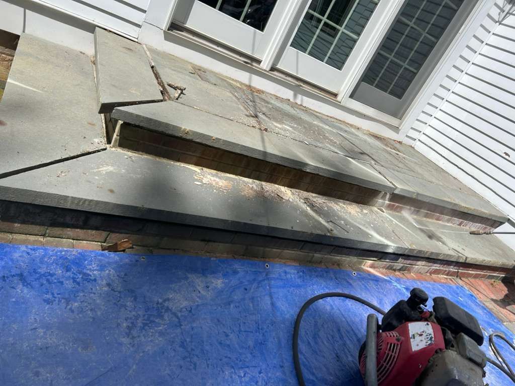 Broken outdoor deck boards with a red power tool on a blue tarp near a house siding