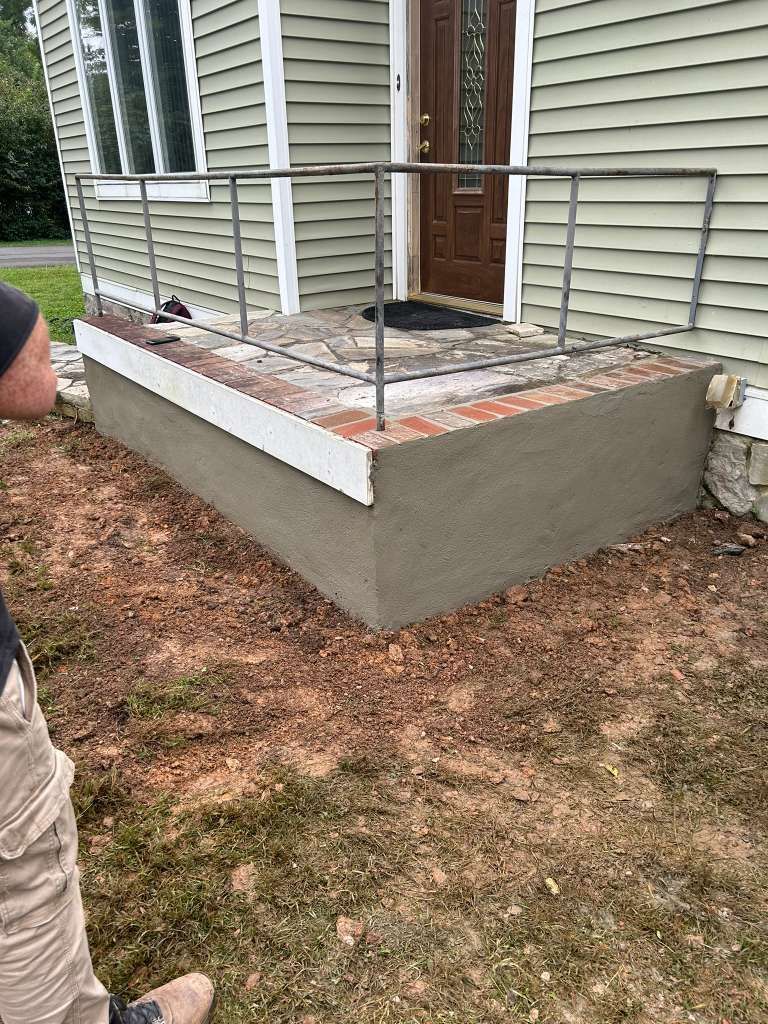 House porch with new concrete base, brick steps, and metal railing beside a yard