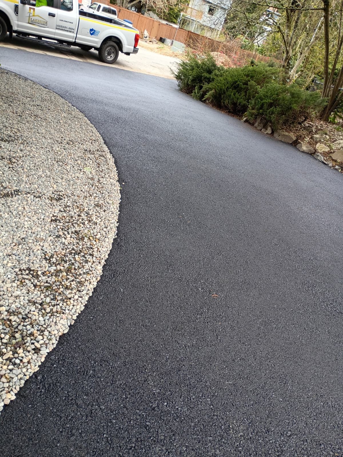 Curved asphalt driveway with gravel edging and shrubs, with a utility truck parked at the top left.