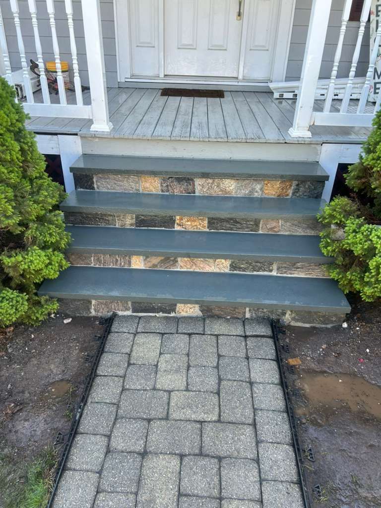 Front porch steps with dark railings leading to a white door, with a stone paver walkway below.