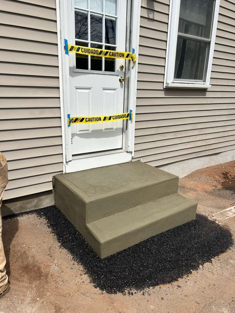 Front door with taped notices, concrete steps, and a black gravel ramp by beige siding.