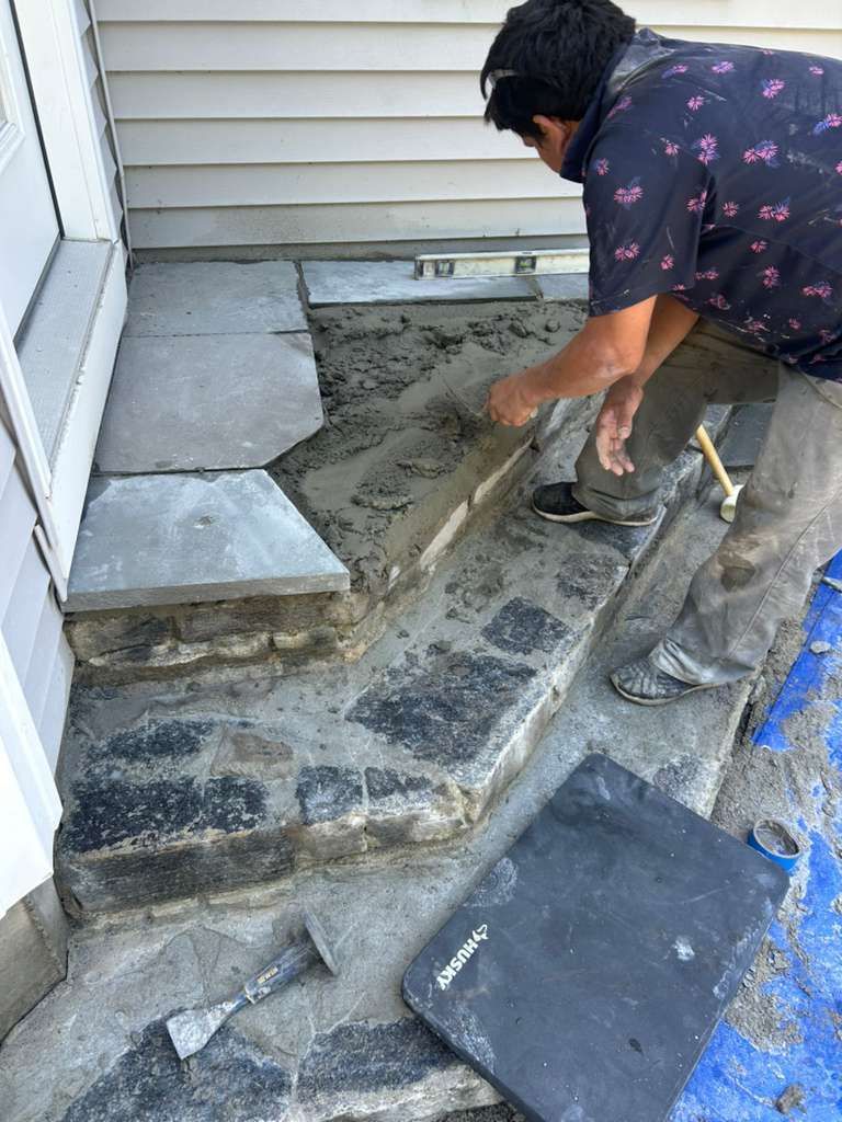 Person smoothing wet concrete on a small front stoop beside a house.