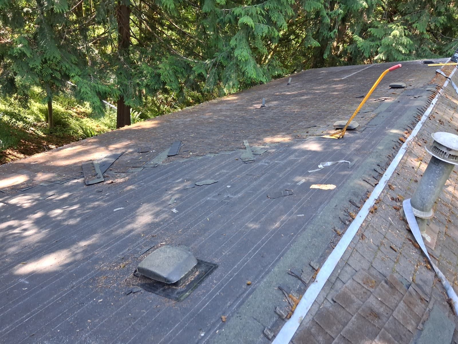 Roof with scattered debris and a loose yellow cable, bordered by trees and a brick wall.