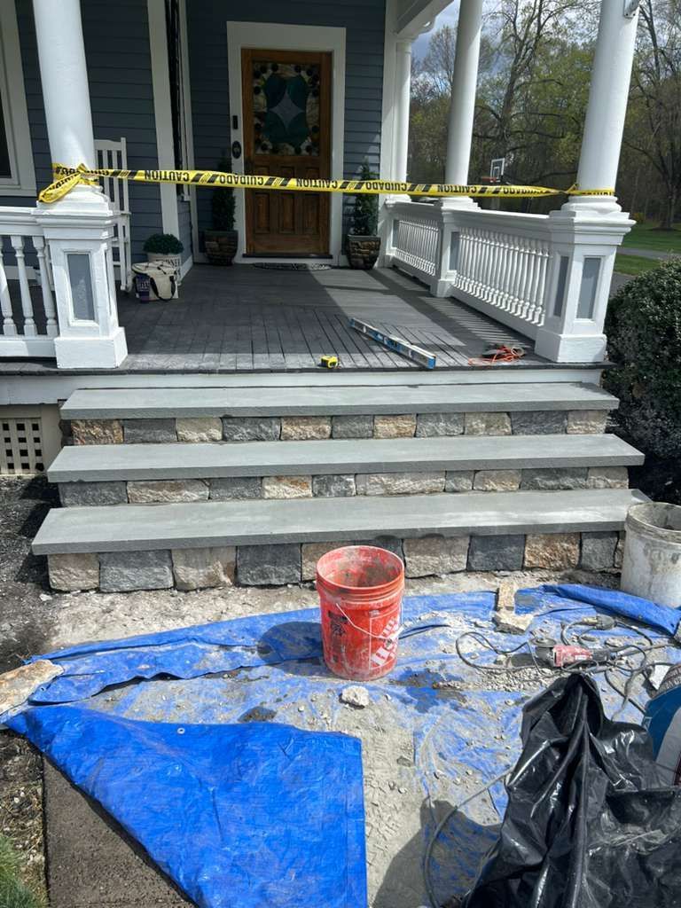 Front porch under repair with caution tape, blue tarp, orange bucket, and debris on steps
