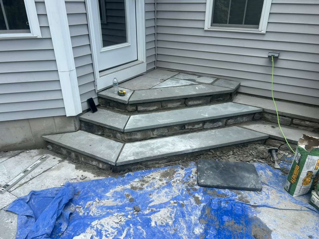 Outdoor concrete steps by a house, with construction materials and a blue tarp in front