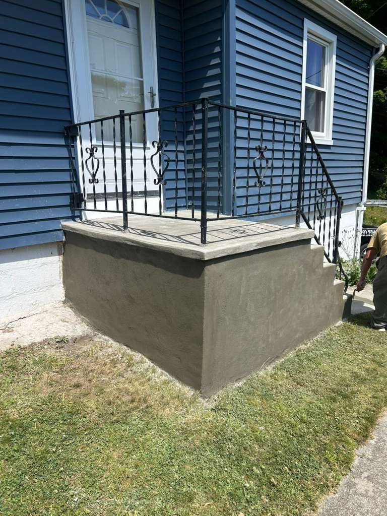 Front porch with blue siding, concrete steps, and black metal railings beside a lawn