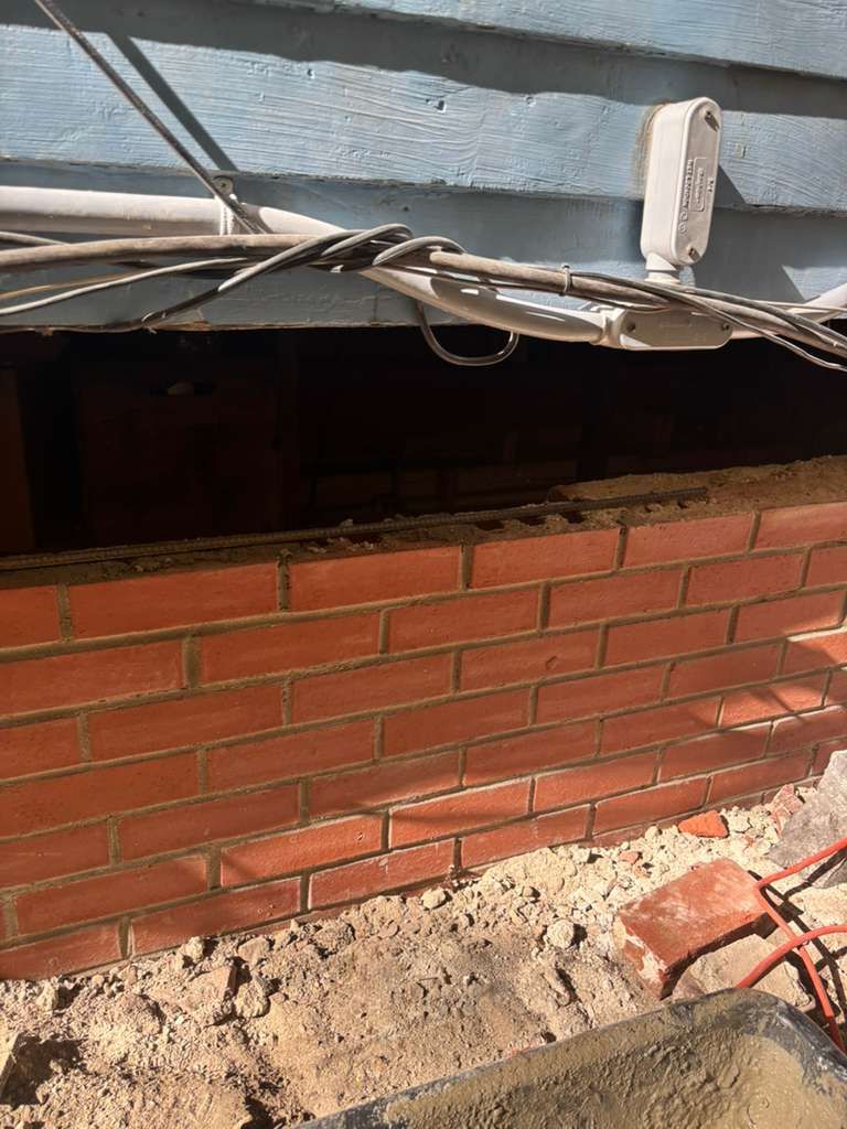 Damaged brick wall under a bent metal roof, with rubble and debris at the base