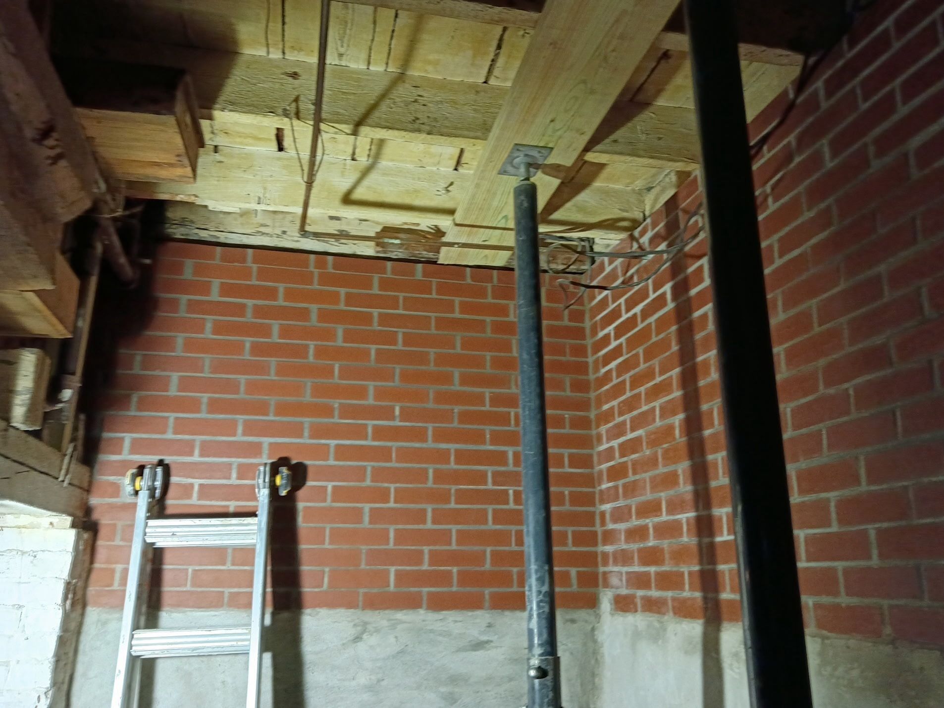 Basement with brick walls, exposed ceiling joists, and a ladder leaning against the wall