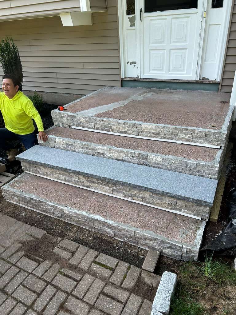 Broken front steps leading to a white house entrance, with a worker in a yellow shirt at left