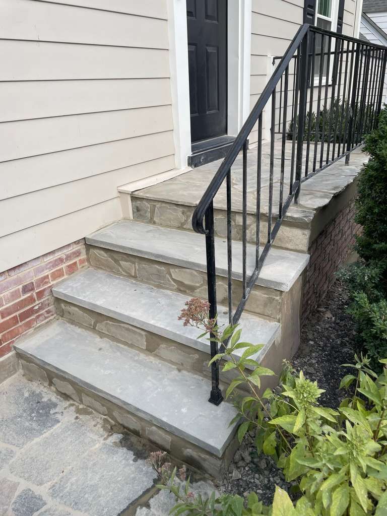 Concrete front steps with black metal railing leading to a house entrance beside beige siding.