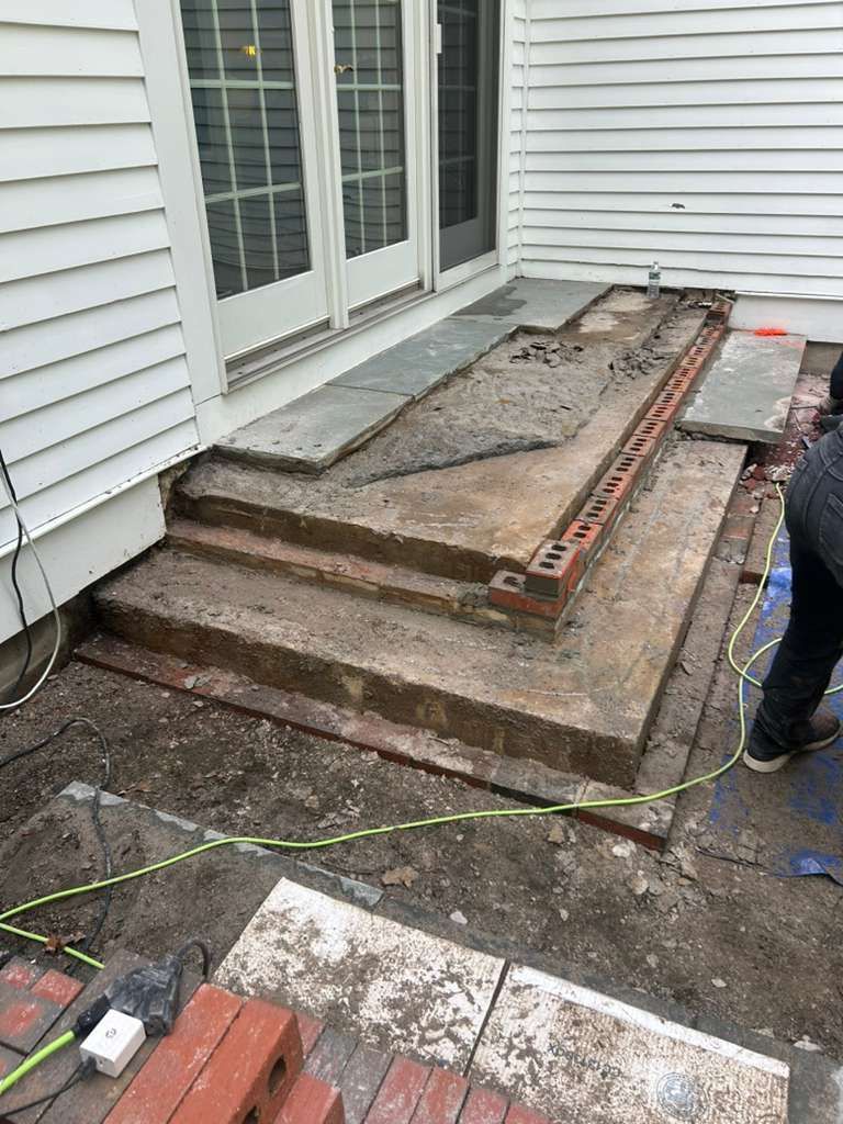 Damaged front stoop with broken concrete steps and exposed brick beside a white house
