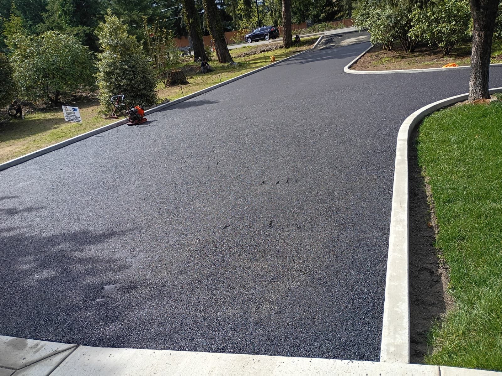 Curved freshly paved asphalt driveway with white edging, bordered by grass and trees