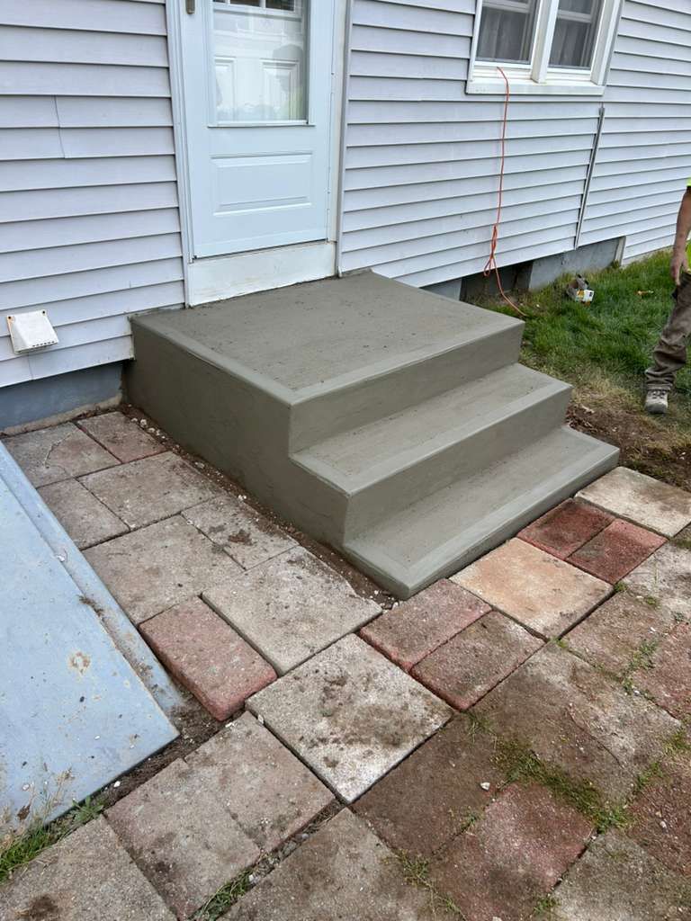 Concrete step platform by a house door, with sloped sides and tiled patio stones in front