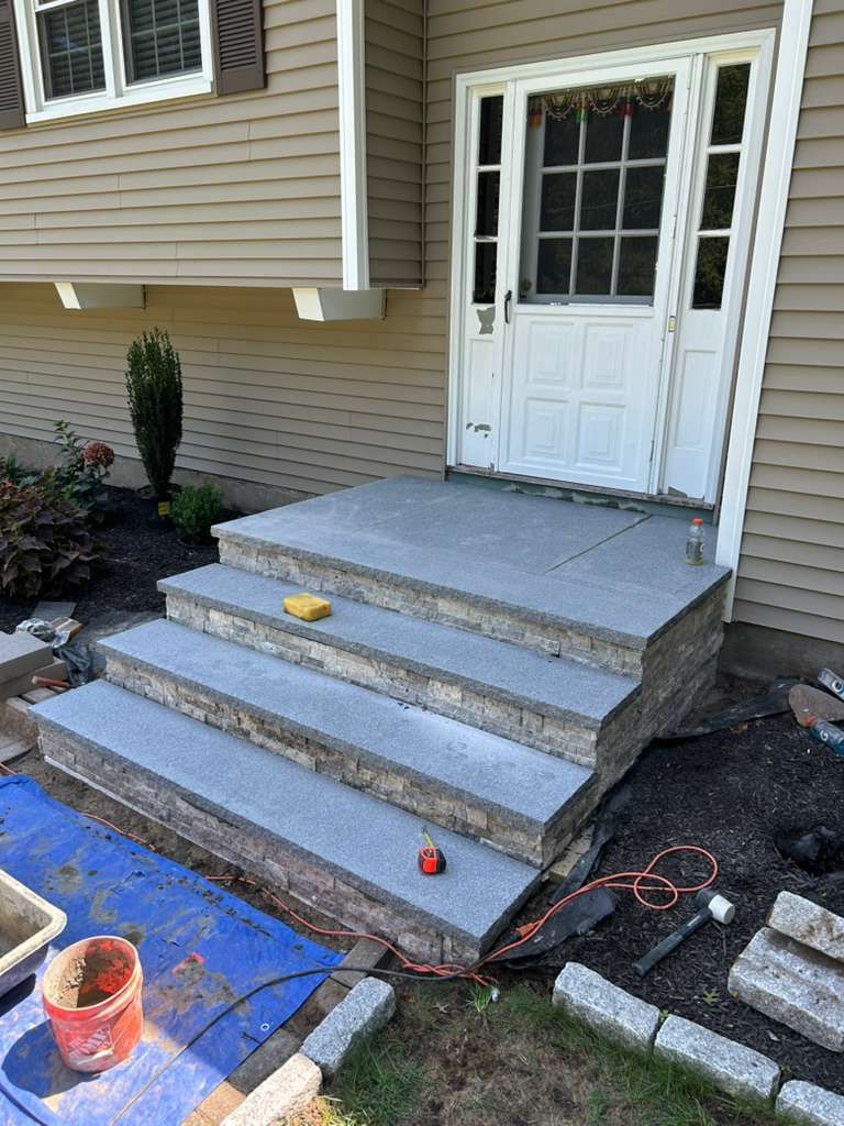 Front porch stairs under repair with gray concrete steps, blue tarp, tools, and white door entrance