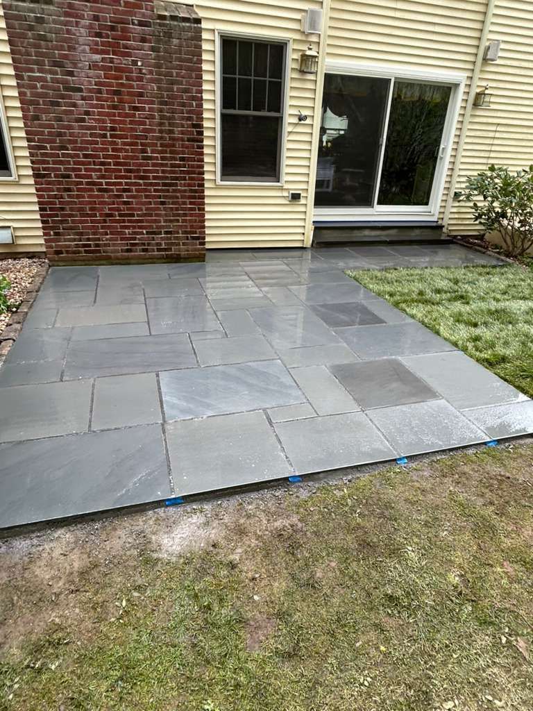 Backyard patio with gray stone pavers beside a house, next to sliding glass doors and a brick wall