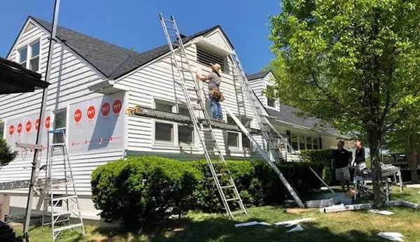Workers on ladders painting a white house exterior on a sunny day